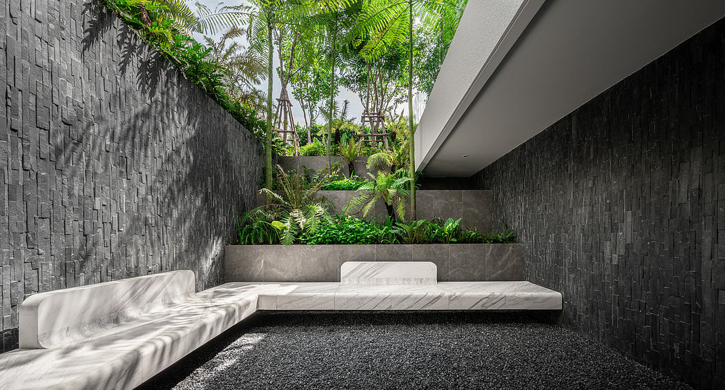 A serene and modern outdoor lounge area with lush foliage, concrete walls, and a minimalist aesthetic.
