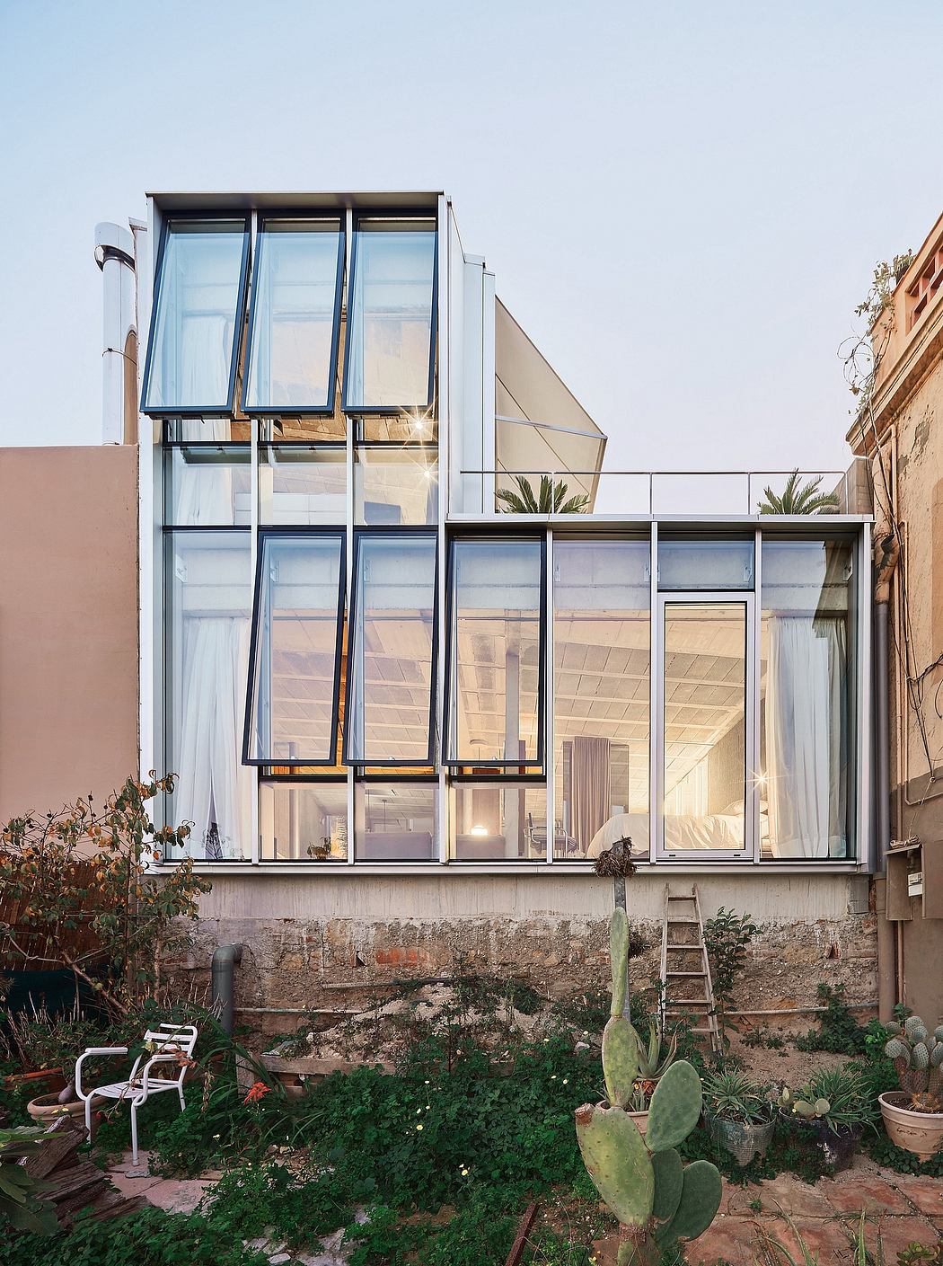 A modern glass facade structure with wooden beams and lush plants in the foreground.