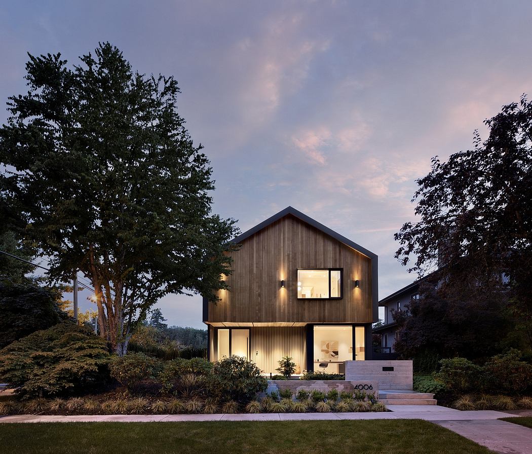 A modern, wooden-clad house with large windows and exterior lighting, set against a natural landscape.