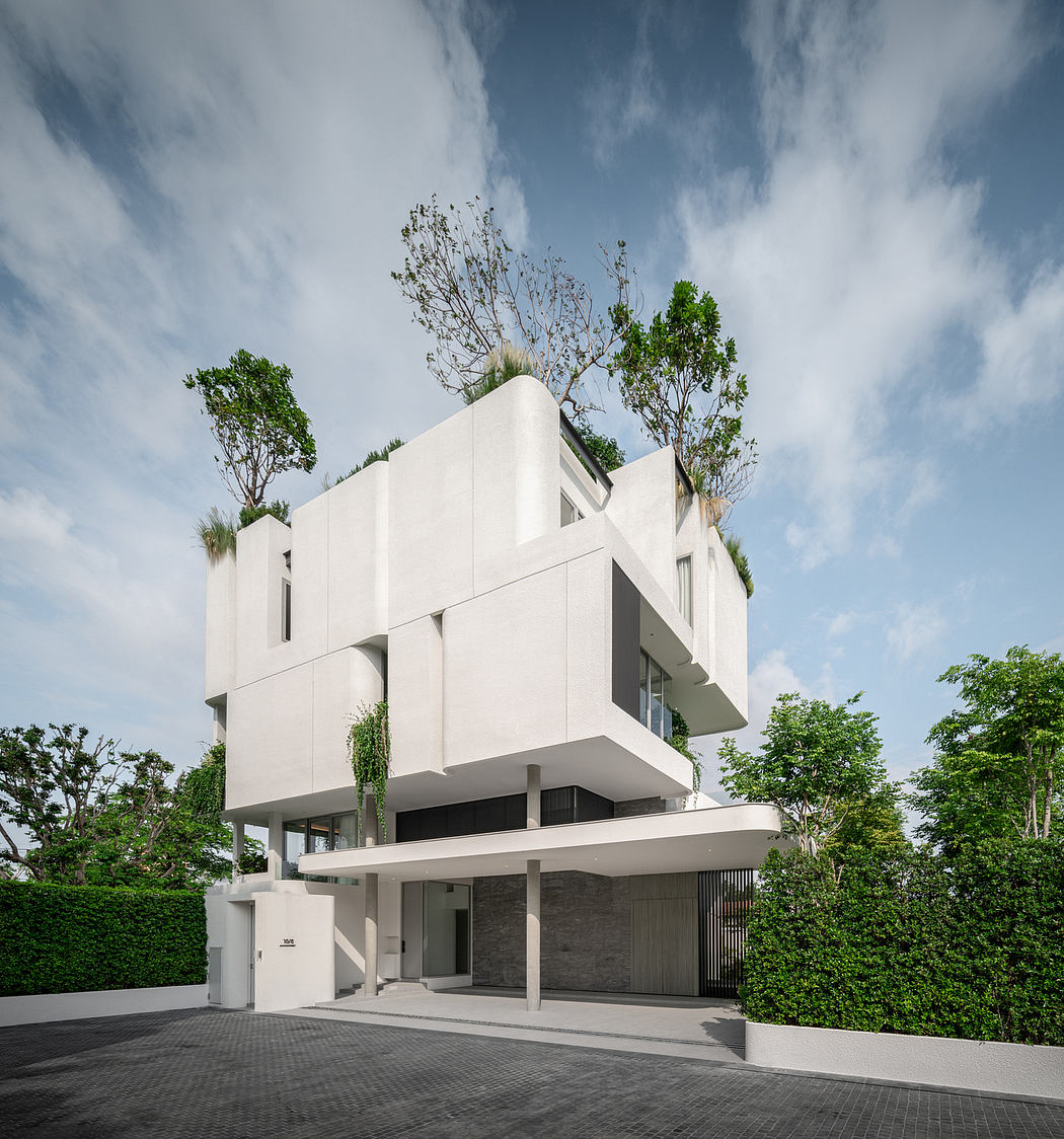Modern white building with geometric design, greenery, and paved entrance.