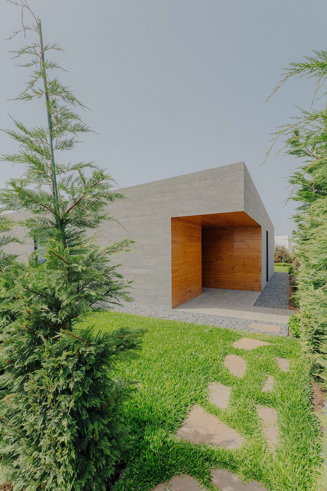 A contemporary concrete structure with a wooden interior, surrounded by lush greenery.
