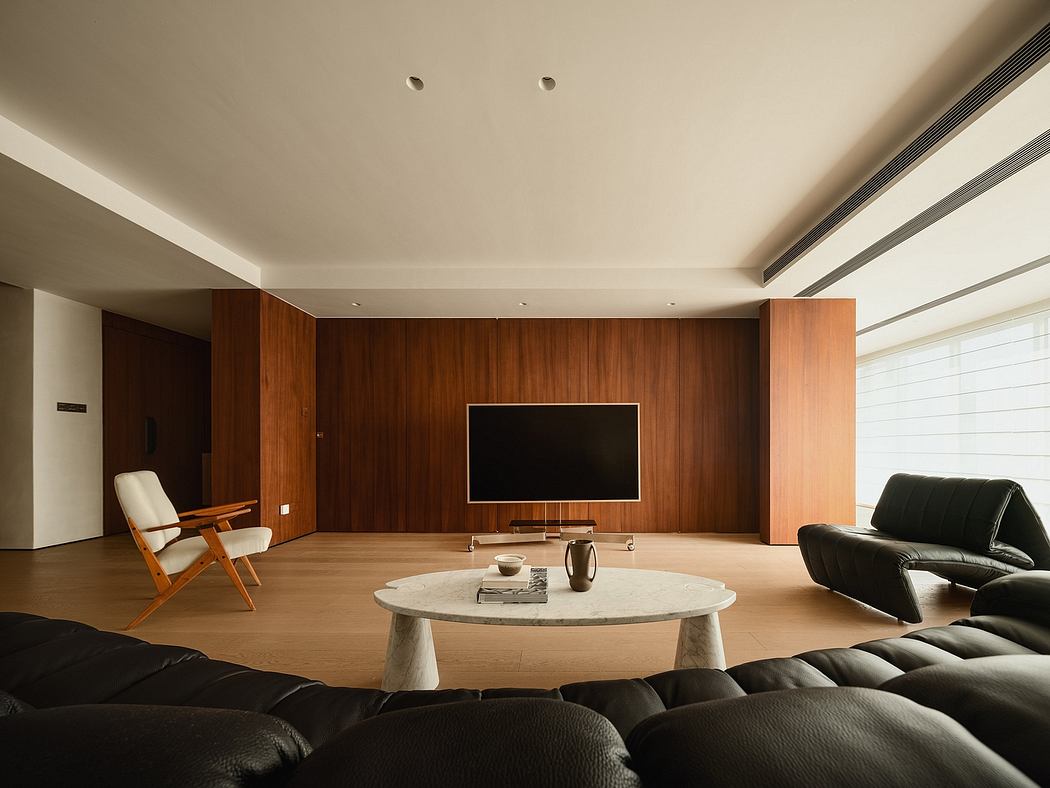 Spacious living room with warm wood paneling, a large TV, and minimalist furniture.