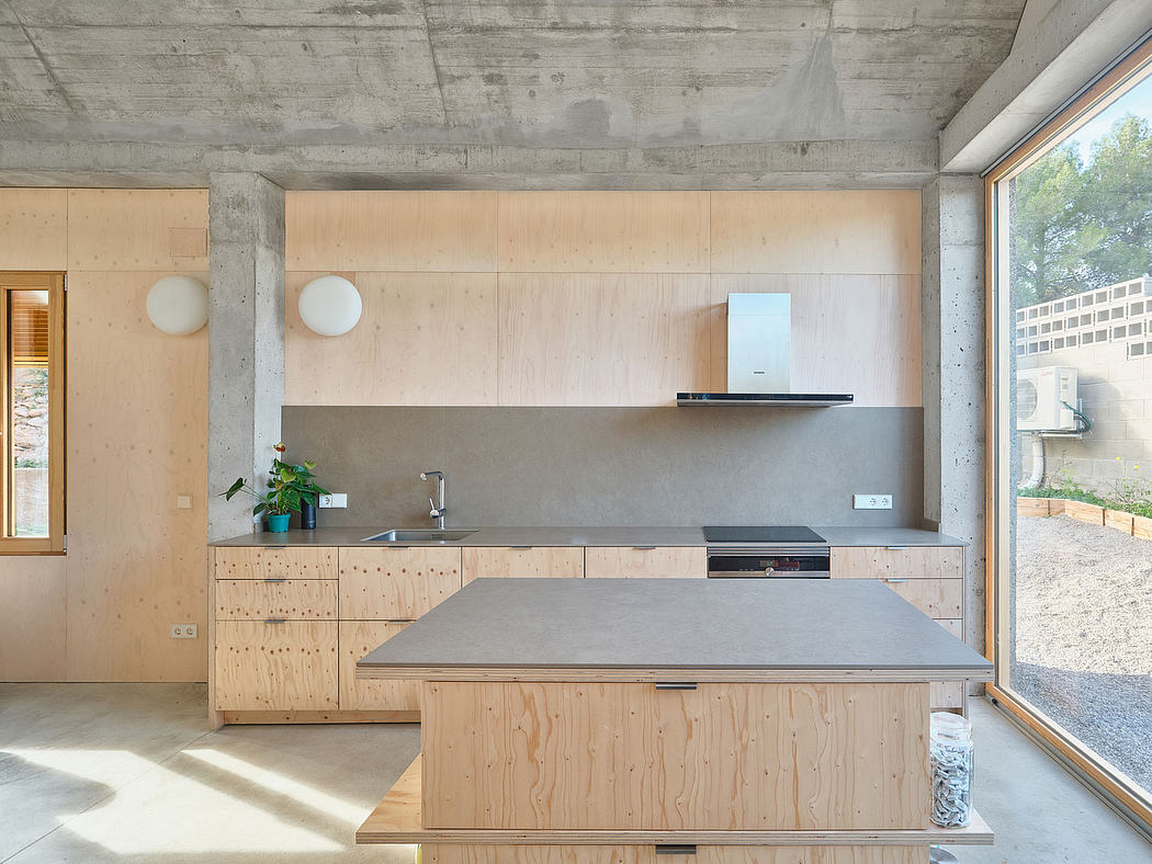 Minimalist kitchen in concrete and natural wood with large sliding windows.