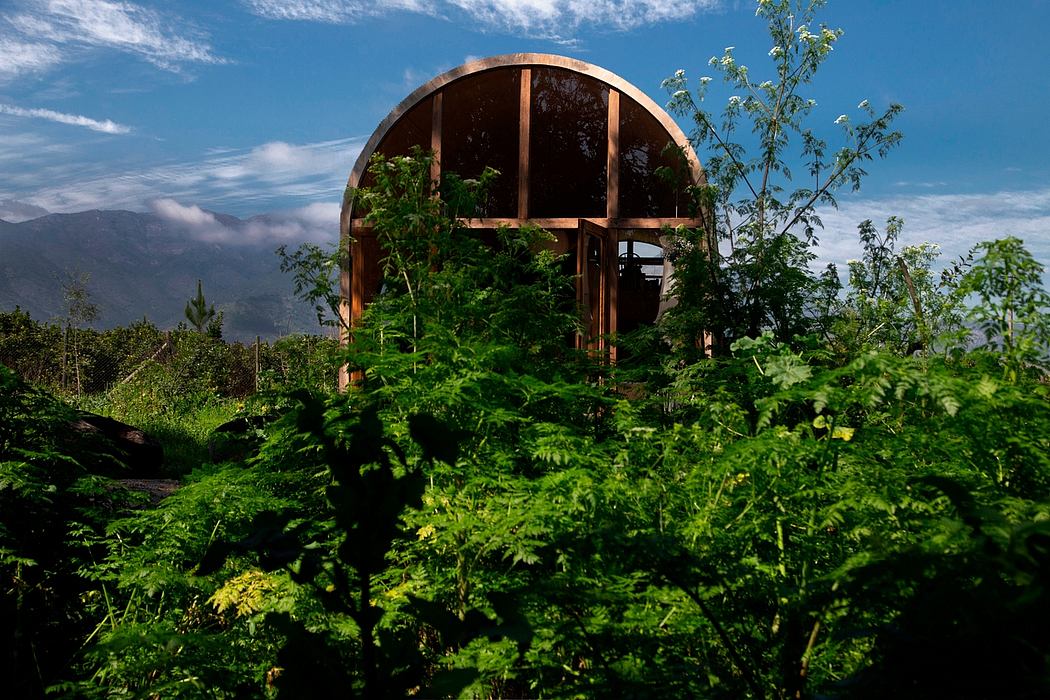 A wooden, half-domed structure nestled among lush, verdant foliage and trees.