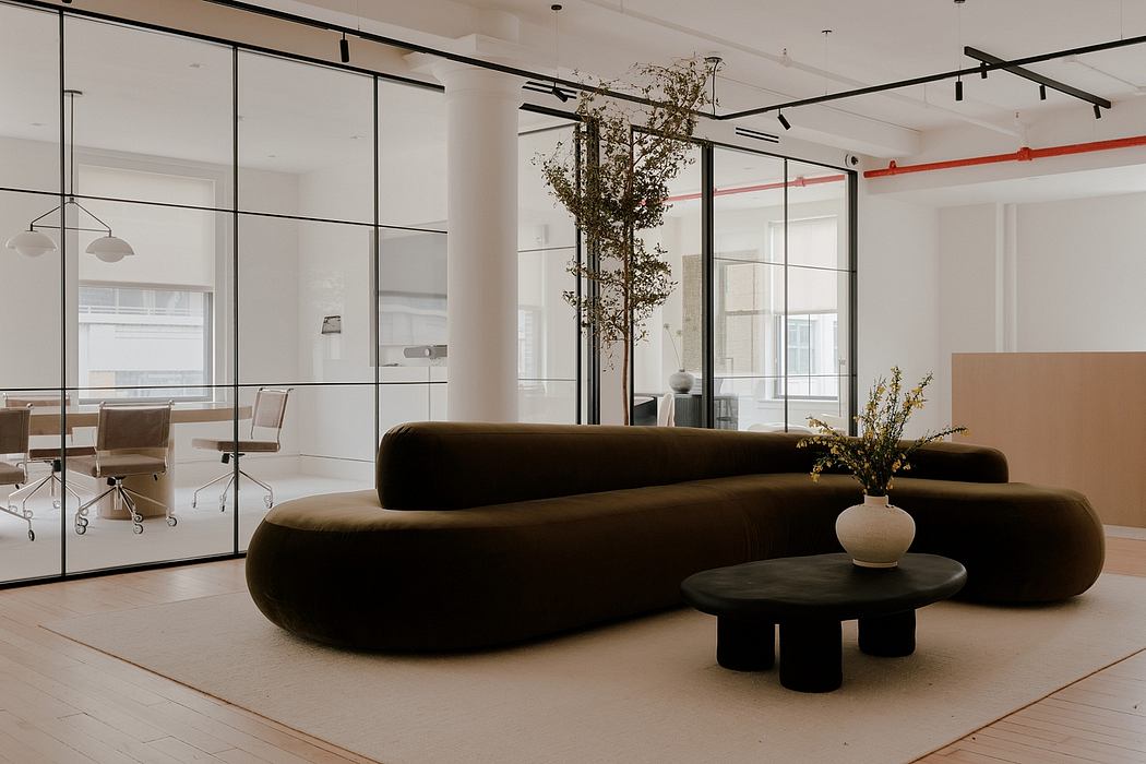 Sleek modern office space with glass partitions, plush brown sofa, and minimalist decor.