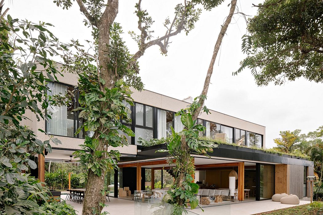 A modern, glass-walled home nestled among lush greenery and large trees, with an open and airy interior.