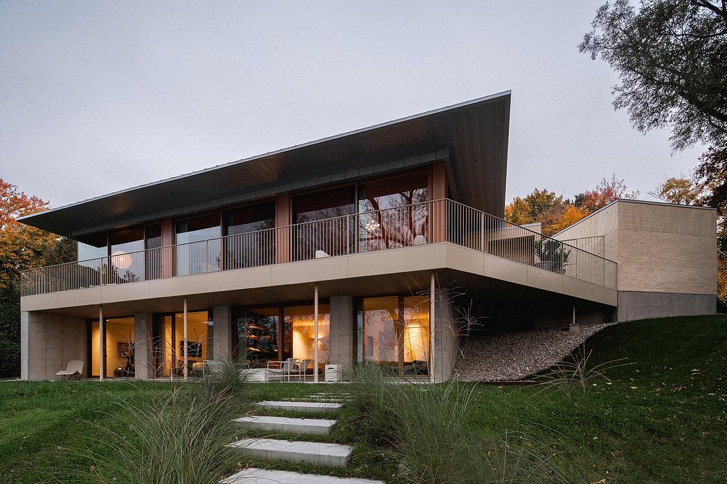 Modern, two-story home with angled roof, glass walls, and exterior balcony overlooking trees.