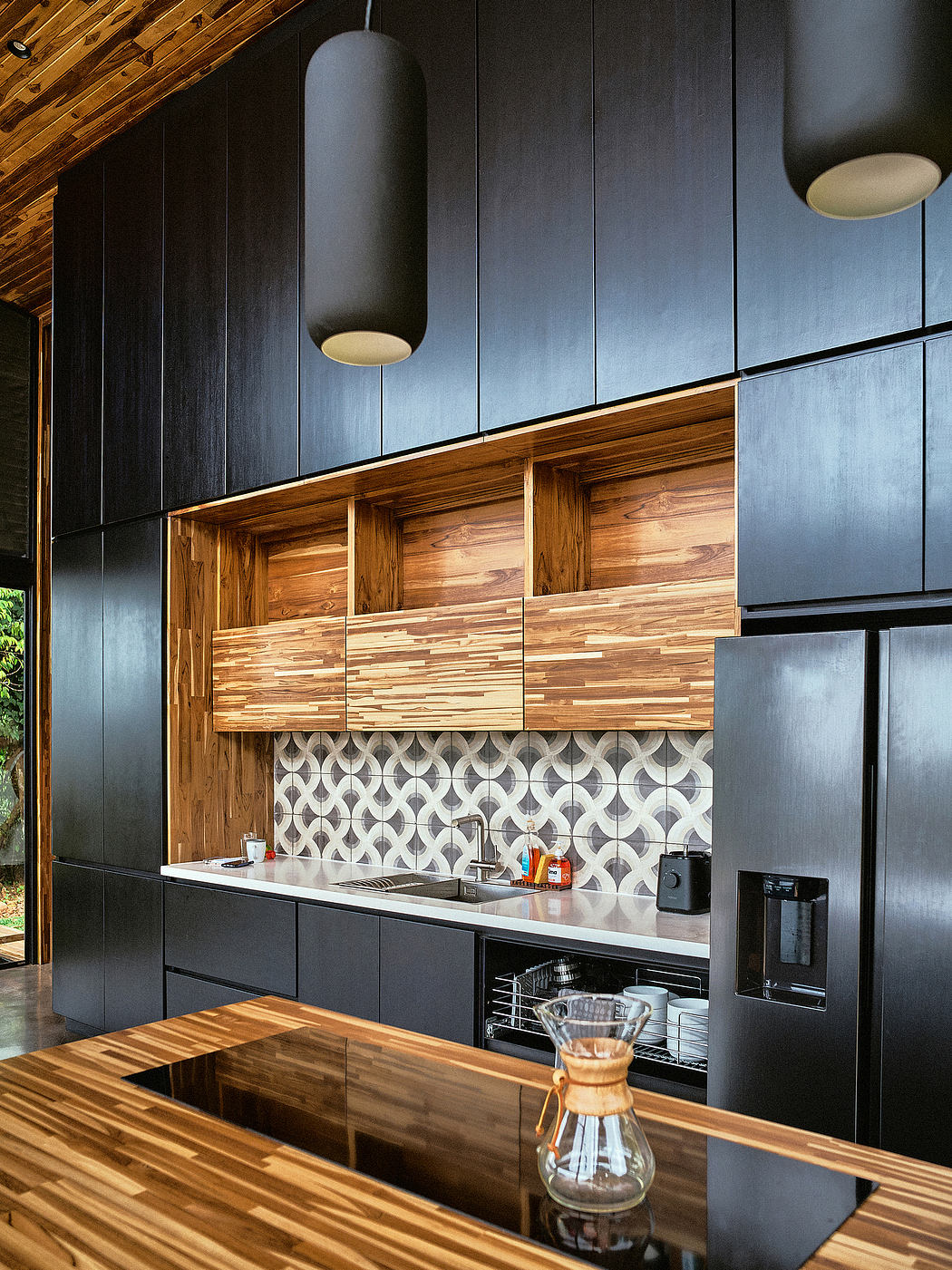 A modern kitchen with a rustic wood and black accent wall, patterned tile backsplash, and sleek cabinets.
