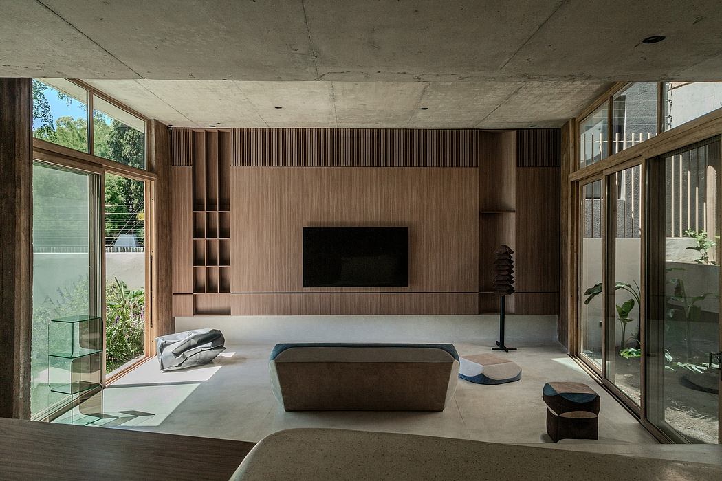 Minimalist concrete and wood living room with floor-to-ceiling windows, built-in shelving, and modern furnishings.