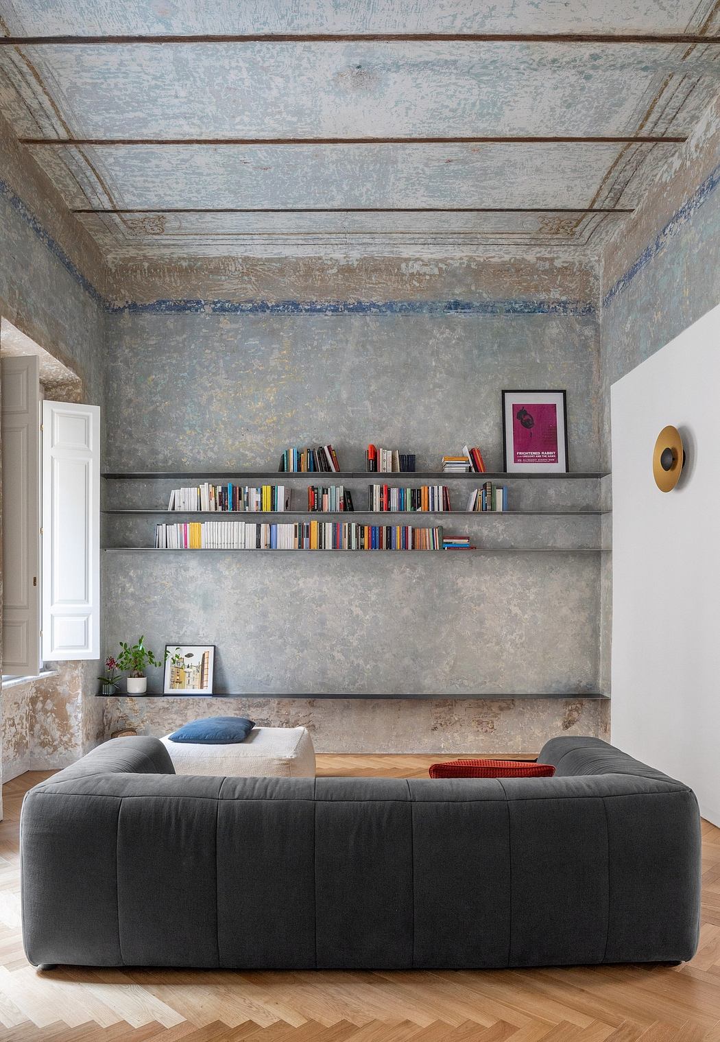 Rustic wall textures, floating bookshelves, and a plush, modular sofa create a cozy, eclectic space.