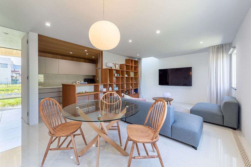 Modern and airy living space with wooden furniture, built-in shelving, and a glass-topped dining table.
