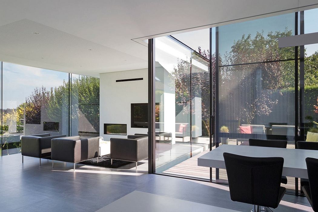 Modern, minimalist interior with expansive glass walls, sleek furniture, and lush garden views.