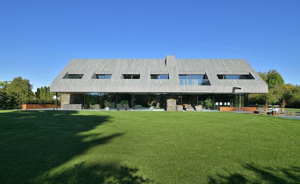 Modern, asymmetrical building with large windows, surrounded by lush greenery and a spacious lawn.