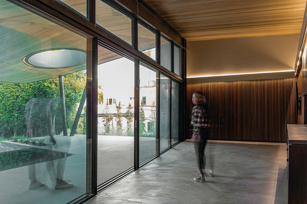 A spacious indoor area with wooden paneling, a glass wall, and a person walking through.