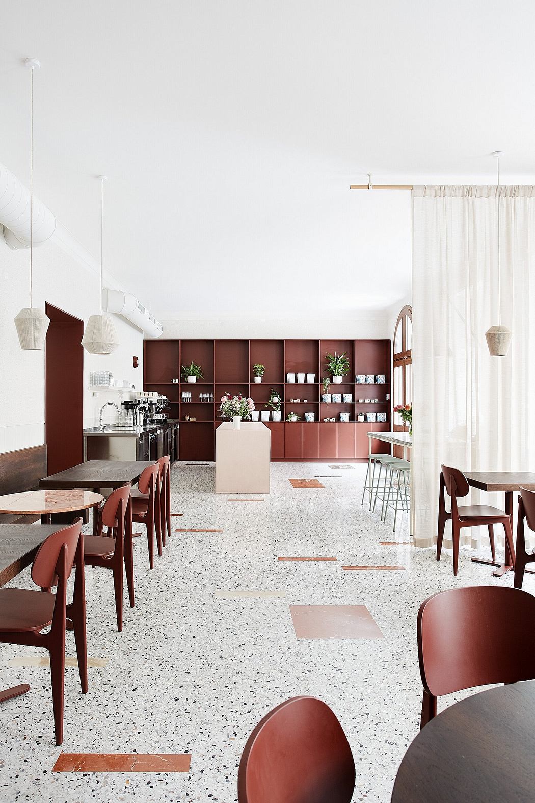 Minimalist cafe interior with burgundy cabinets, terrazzo flooring, and pendant lighting.