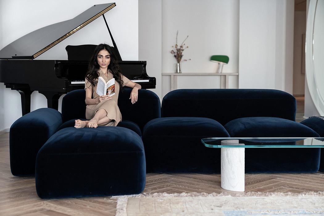 Black grand piano, plush navy sofas, glass-topped table, and a plant decoration against a light wall.