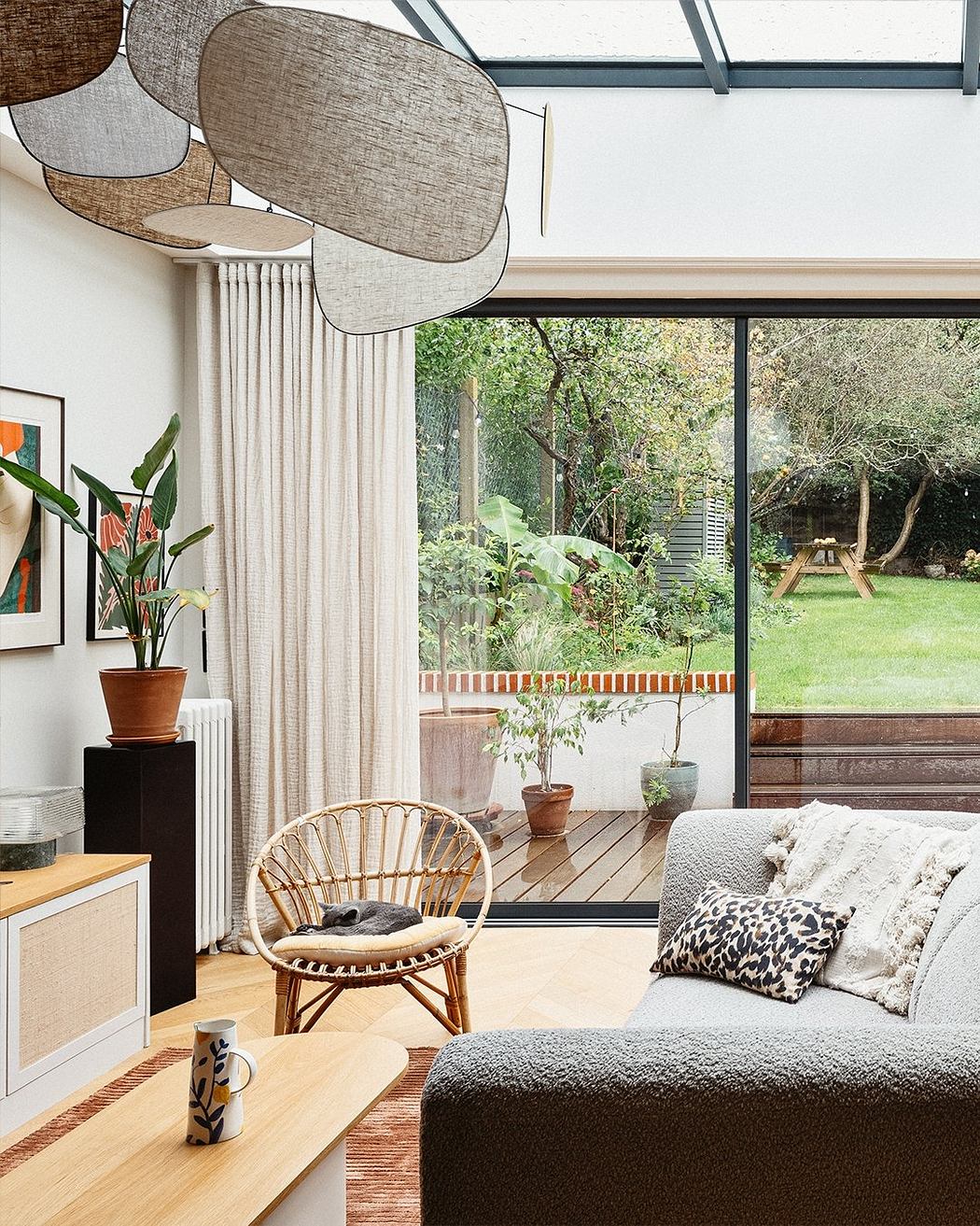 Cozy living room with large windows overlooking a lush garden, featuring modern furniture and natural elements.