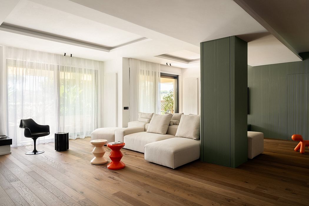 Modern, open-concept living room with white sectional sofa, wooden floors, and bold green pillar.