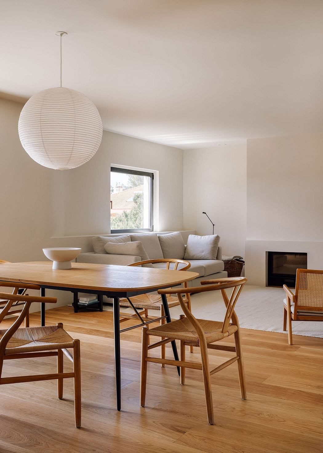 Minimalist living room with wooden dining table, chairs, and a large white pendant lamp.