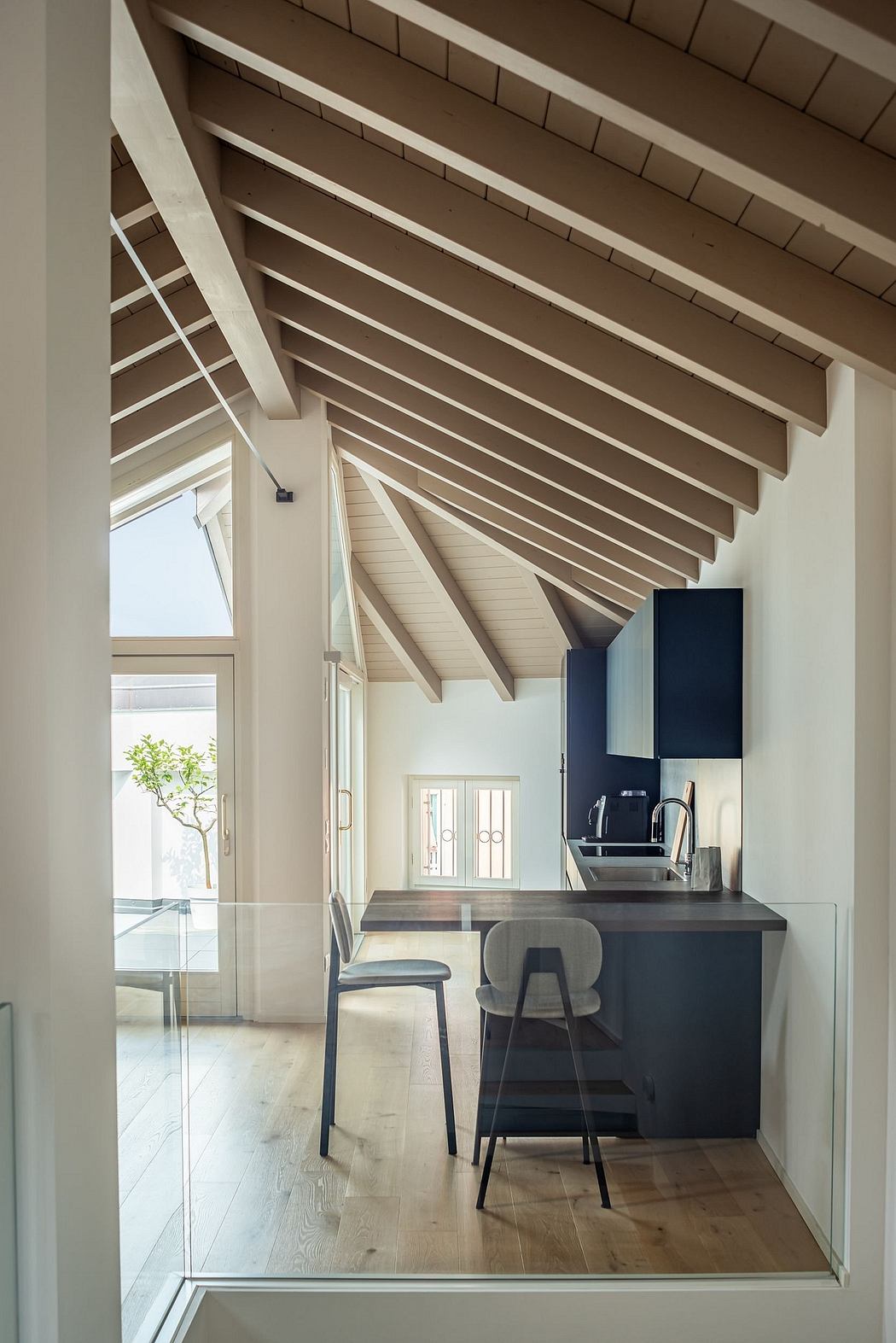 The image shows a modern, open-concept kitchen with a vaulted ceiling and wooden beams.