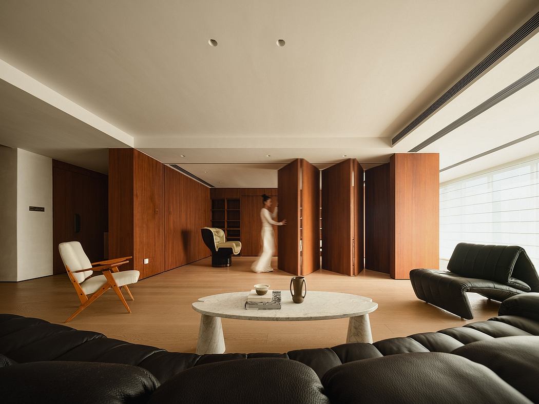 A spacious, modern living room with wooden walls, built-in furniture, and a round marble coffee table.