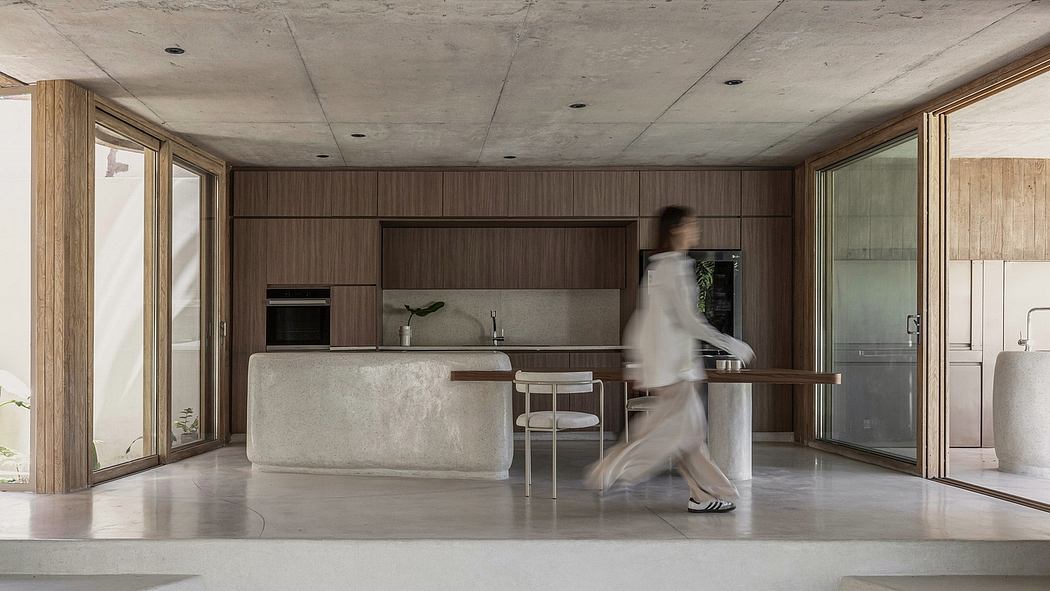 Spacious kitchen area with modern wood-paneled walls and concrete flooring. Blurry figure in motion.