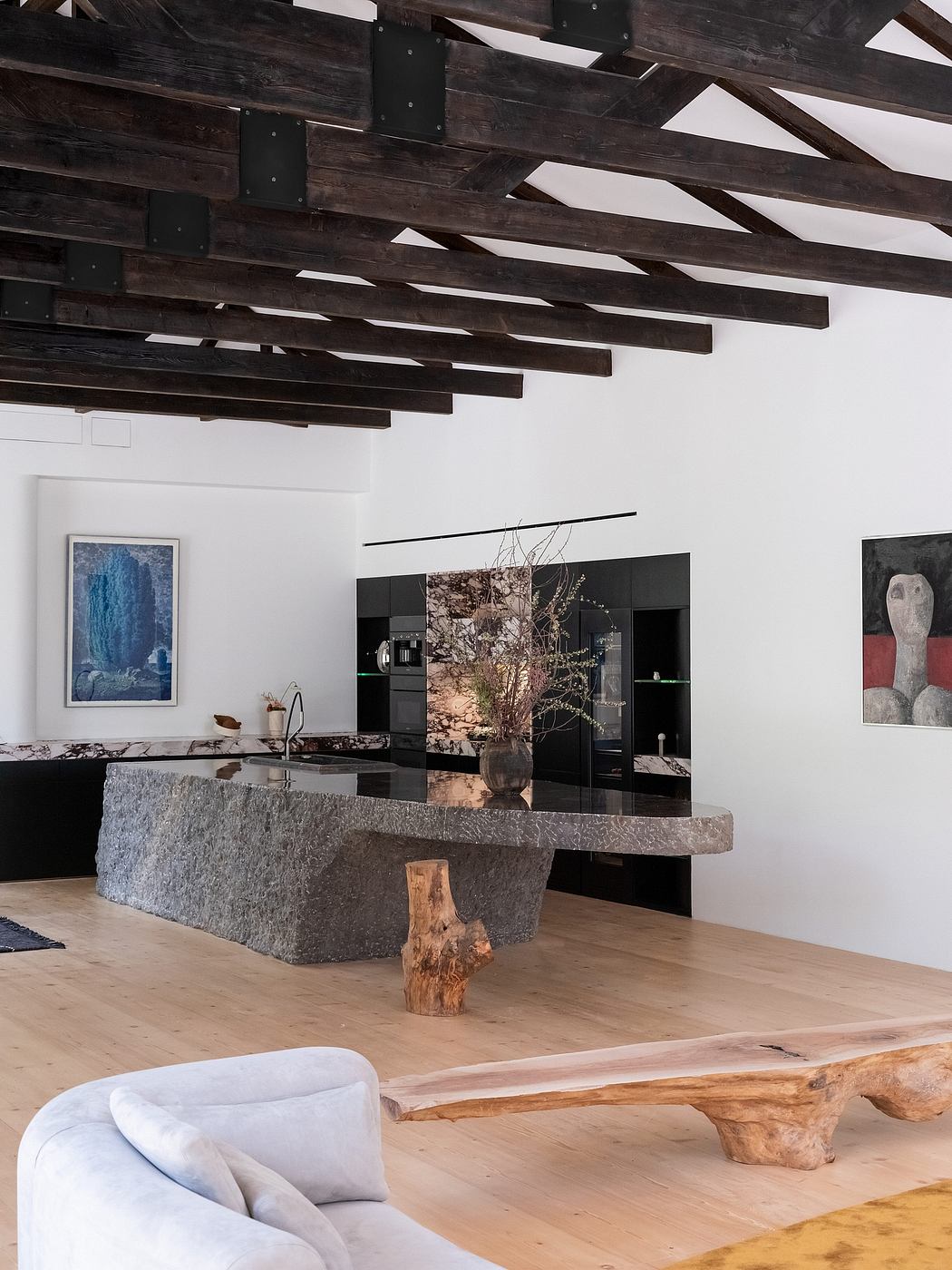 A modern, rustic kitchen with sleek black cabinetry, natural wood beams, and stone countertops.