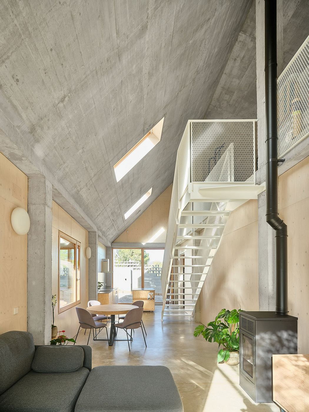Open-concept living space with concrete walls, modern furniture, and lush greenery.