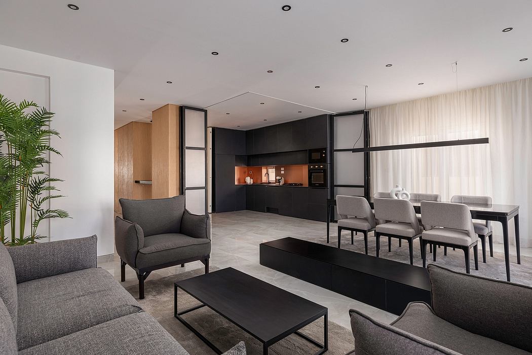 A modern, minimalist living room with a sleek black kitchen, plush gray furniture, and a dining area.