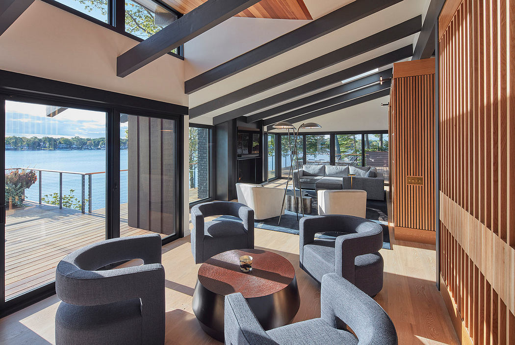 High-ceilinged open-plan living space with wood beams, seating, and panoramic waterfront views.