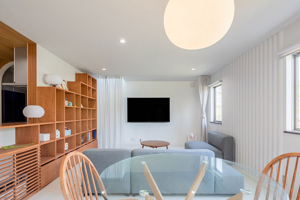 A modern, minimalist living room with a large storage wall, couch, and circular glass table.