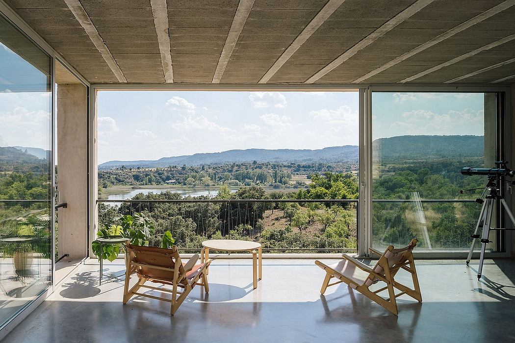 Expansive panoramic vista framed by concrete ceiling beams, glass walls, and minimalist furniture.
