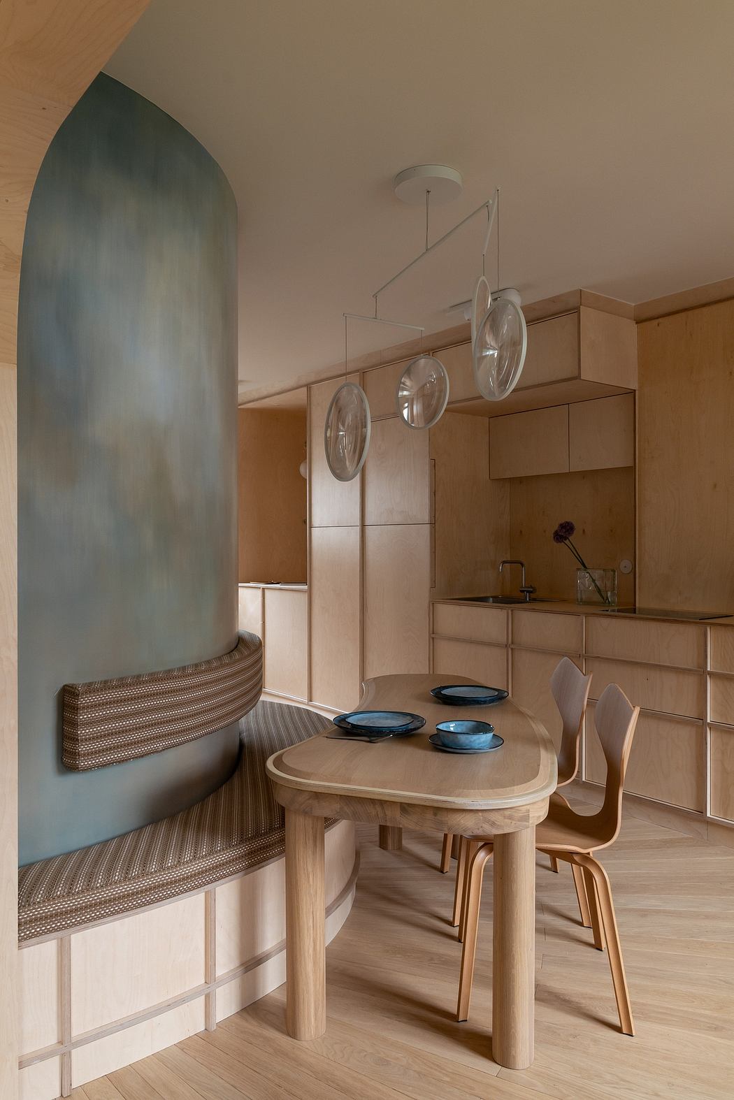 An elegant dining area with a curved upholstered banquette, wooden table, and pendant lights.