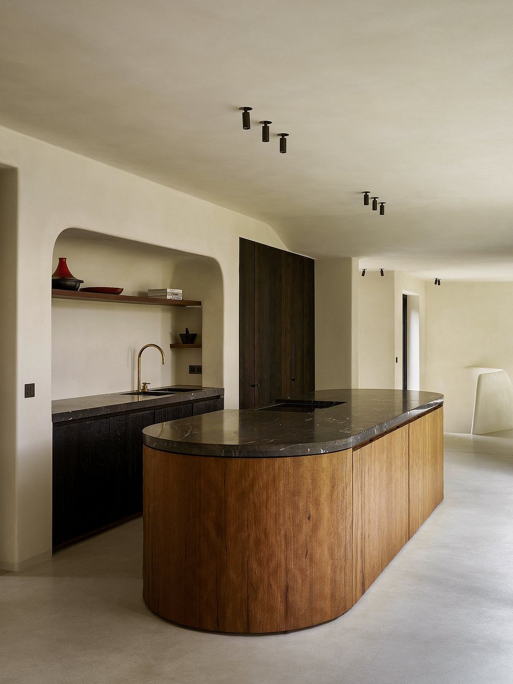 A modern kitchen with a curved wooden island, dark marble countertops, and recessed lighting.