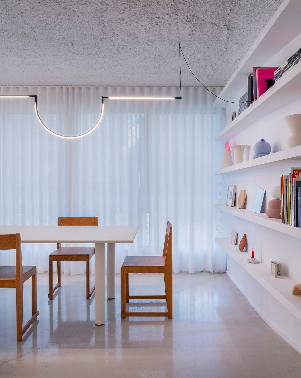 Modern dining area with wooden furniture, minimalist shelving, and curved lighting fixture.