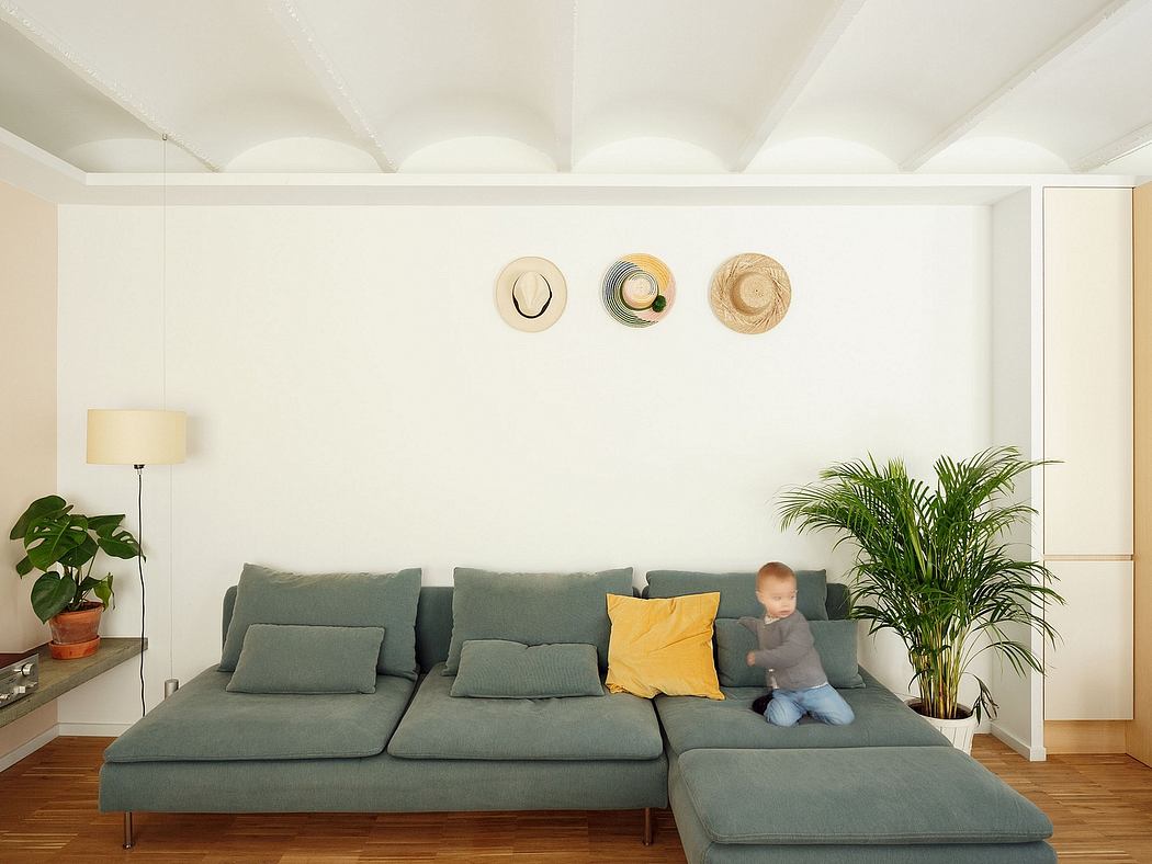 Spacious living room with white walls, gray modular sofa, potted plants, and decorative wall hats.