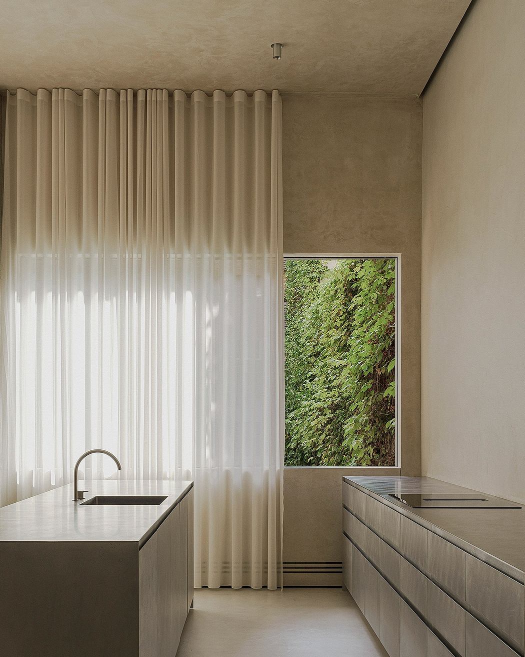 Modern, minimalist kitchen with floor-to-ceiling curtains, built-in cabinets, and a framed window view of lush greenery.