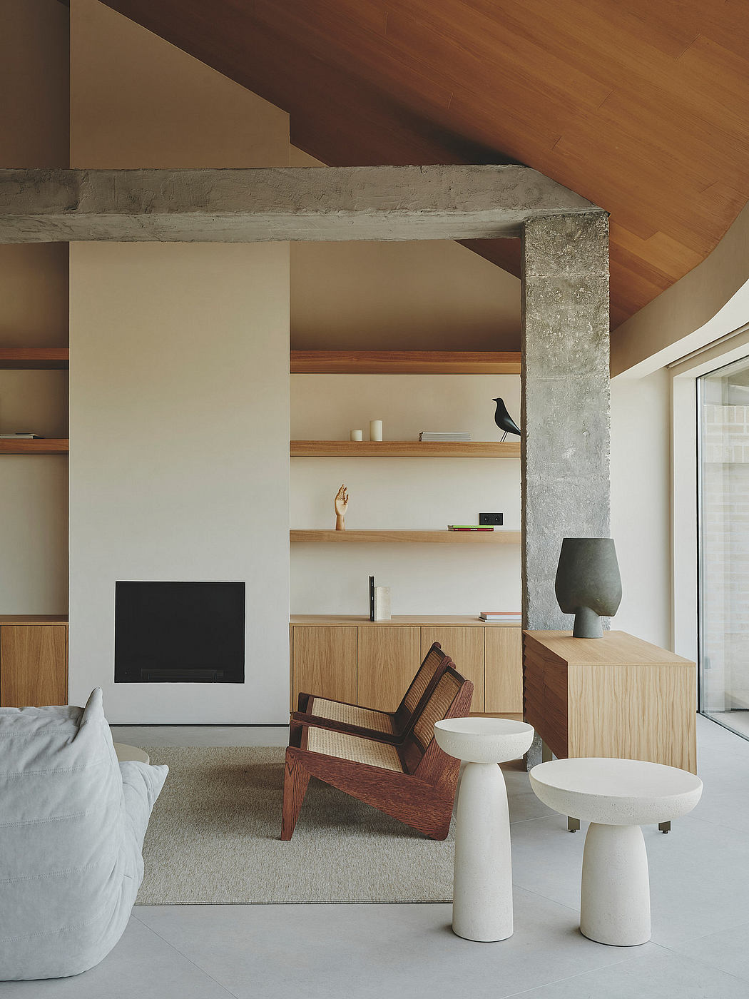 A modern, minimalist living room with concrete beams, wooden shelves, and sculptural furniture.