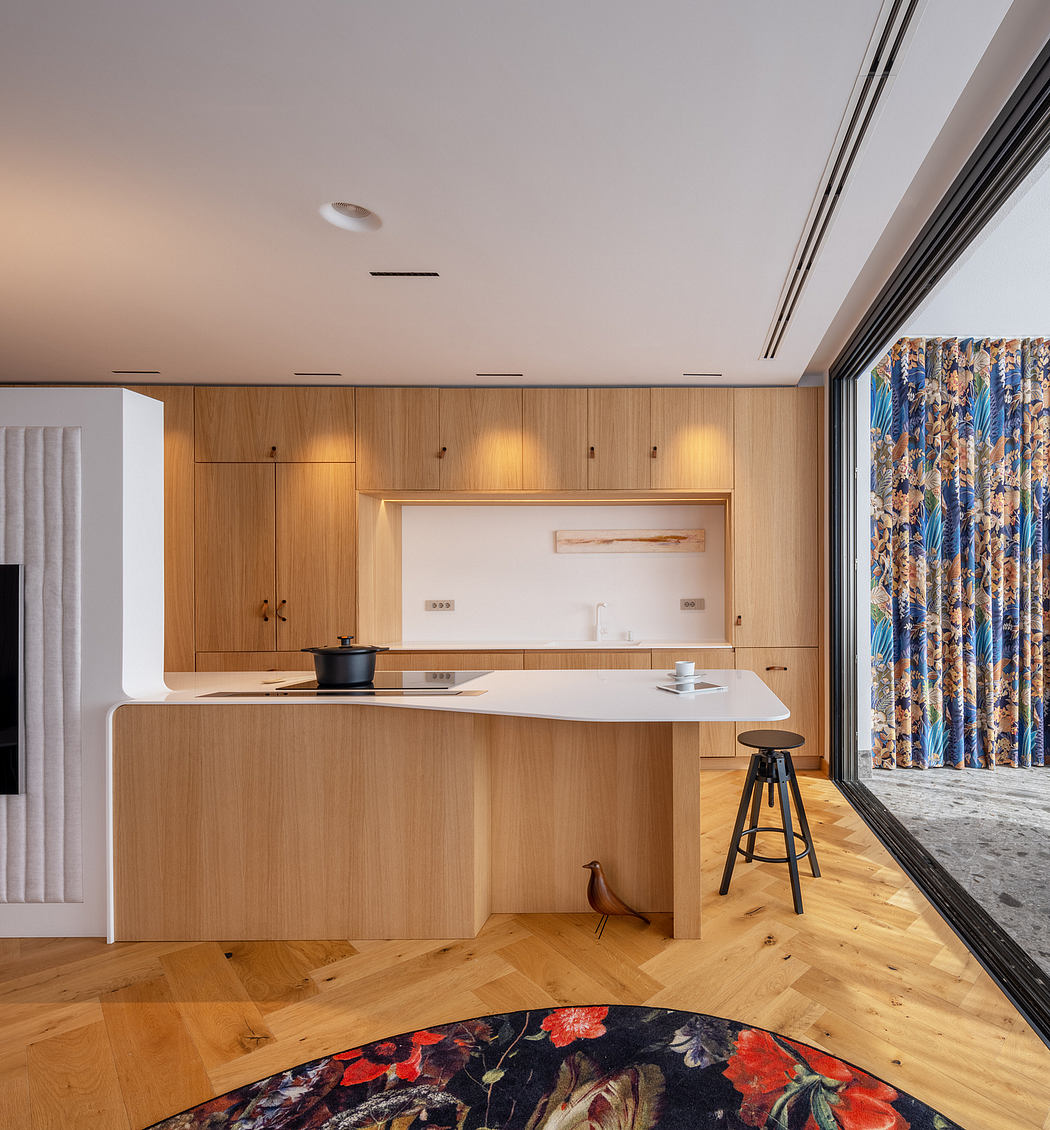 Modern kitchen with wooden cabinetry, white countertop, and vibrant floral curtains.