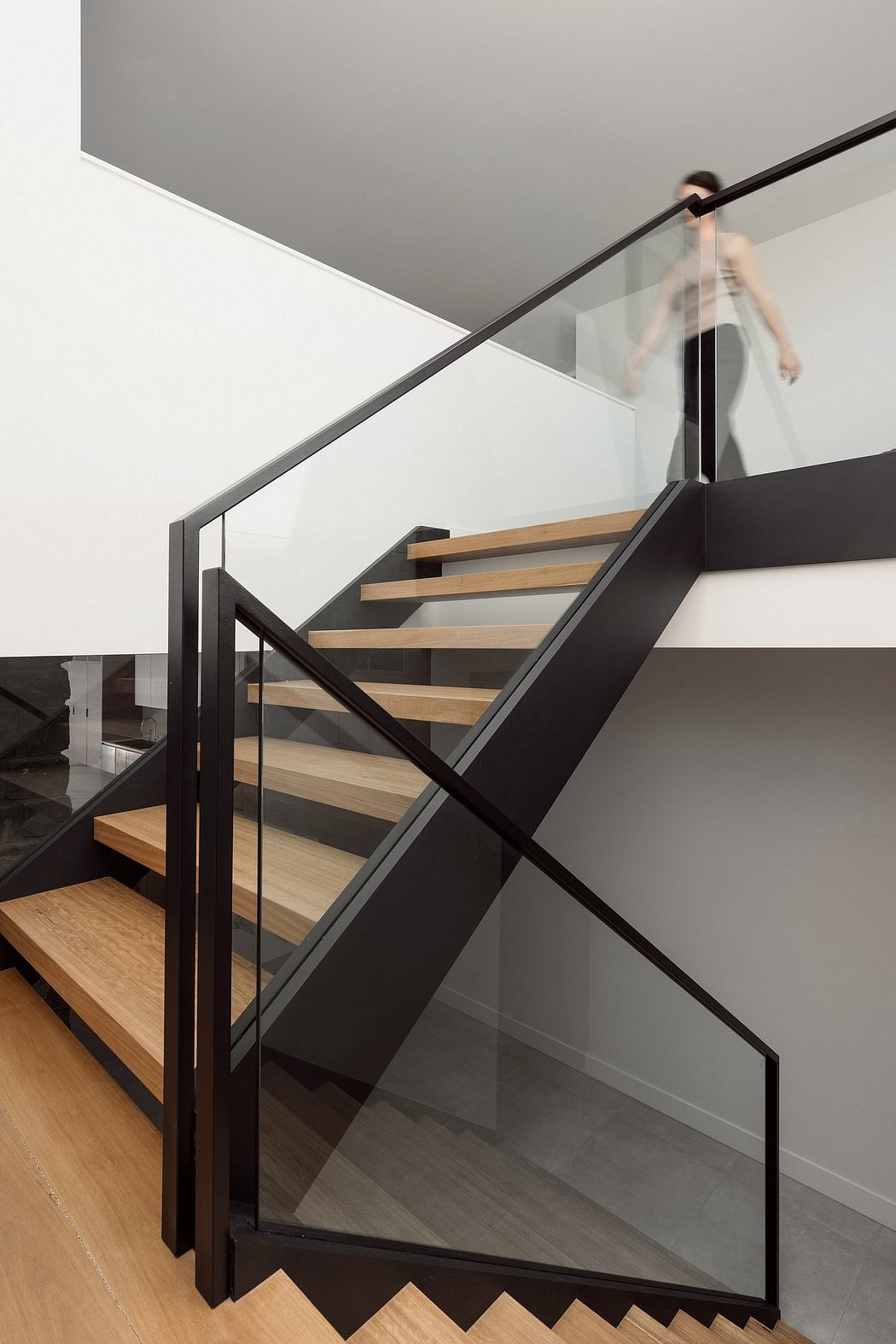 Modern staircase with sleek black metal frame, wooden treads, and glass panels.