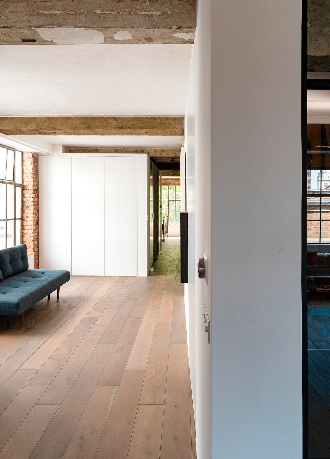 Spacious open-plan room with wood-beamed ceilings, hardwood flooring, and a plush teal sofa.