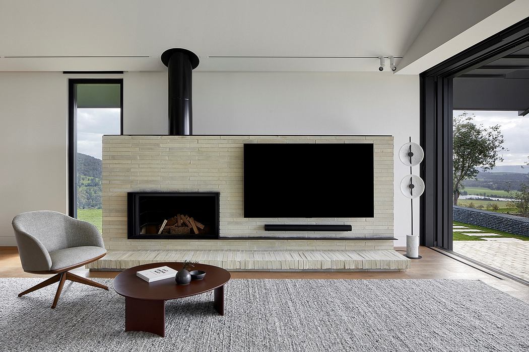 A modern living room with a brick fireplace, TV, and large windows overlooking nature.