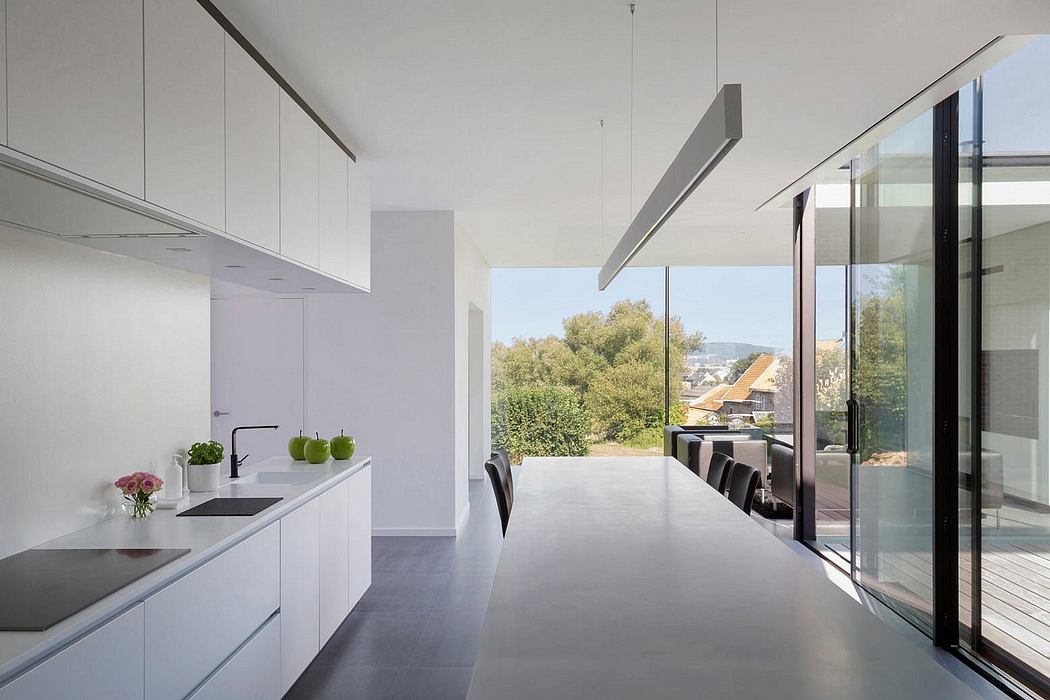 Minimalist kitchen and dining area with large windows overlooking lush outdoor scenery.