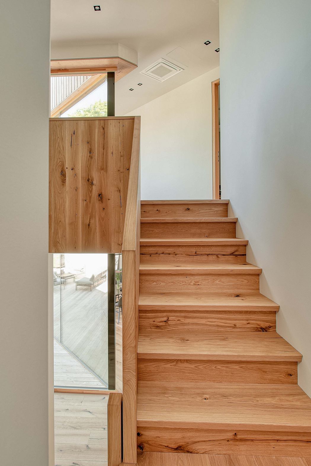 A modern staircase with natural wood finishes and a glass partition, leading to an outdoor view.