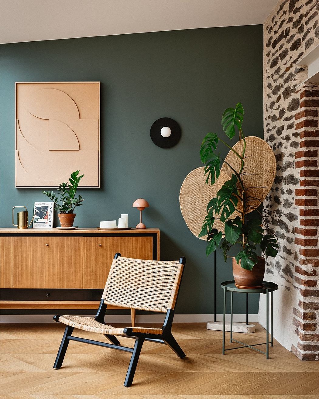 Cozy living room with wooden furniture, geometric decor, and lush greenery against brick walls.