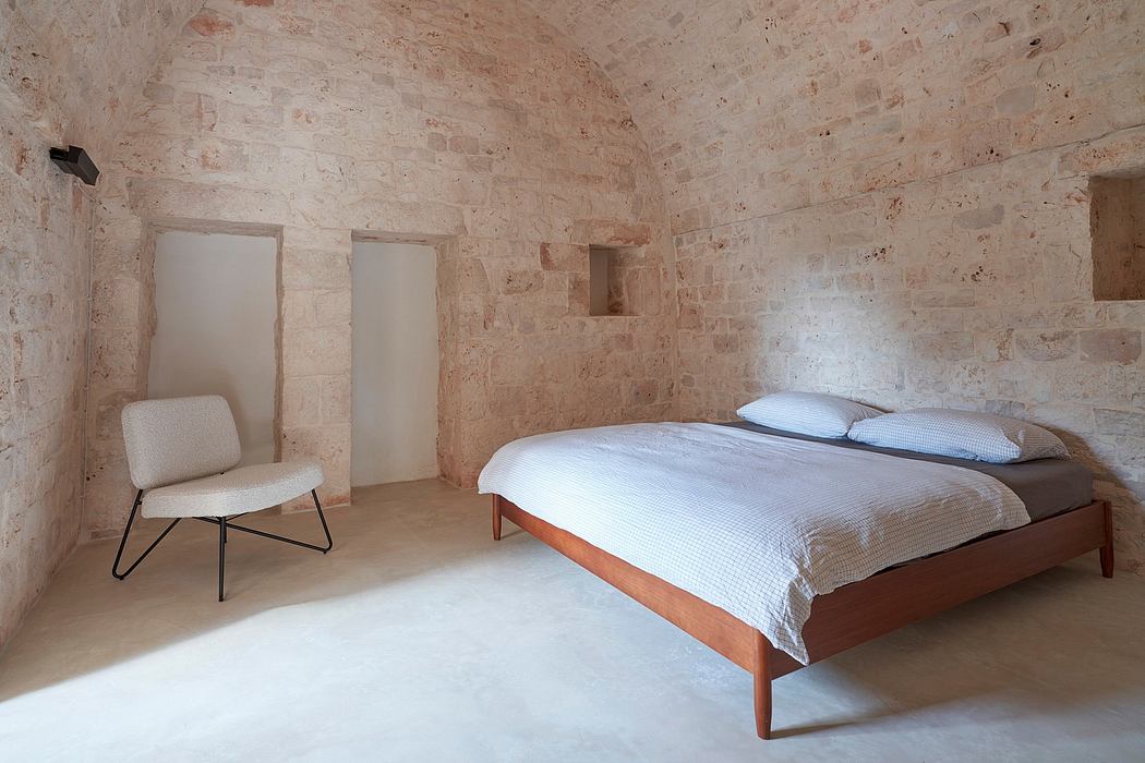 Minimalist bedroom with exposed stone walls, wooden bed frame, and modern upholstered chair.