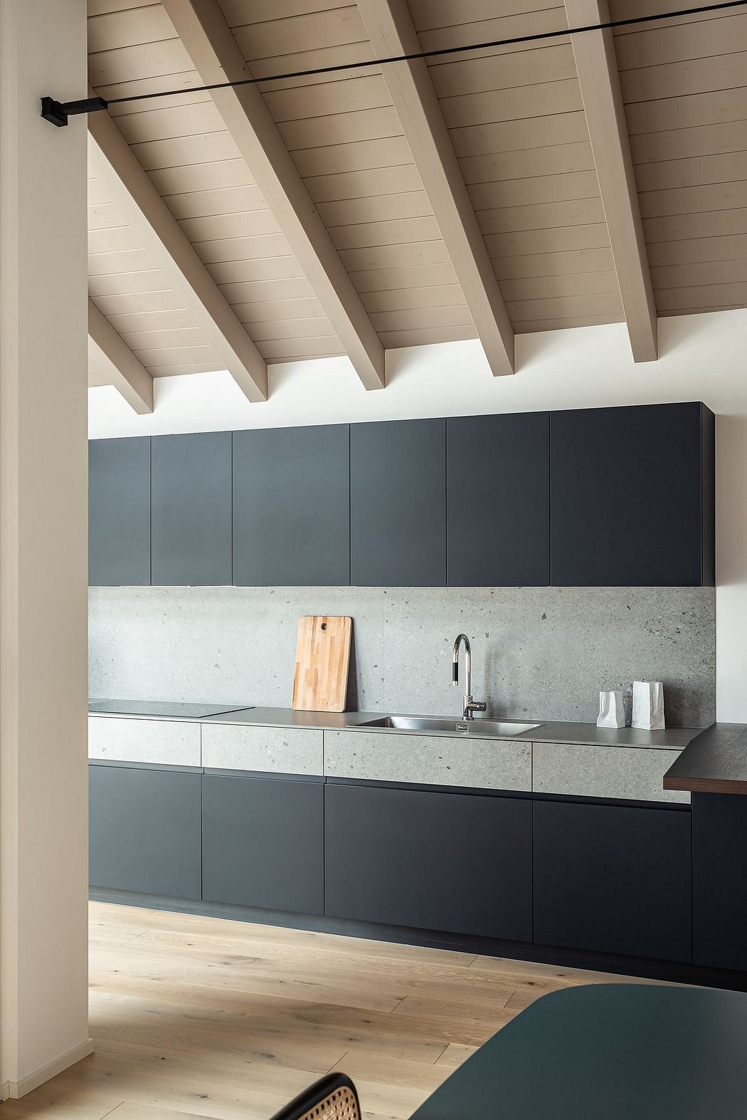 A modern kitchen with sleek gray cabinets, a concrete counter, and an exposed wooden ceiling.