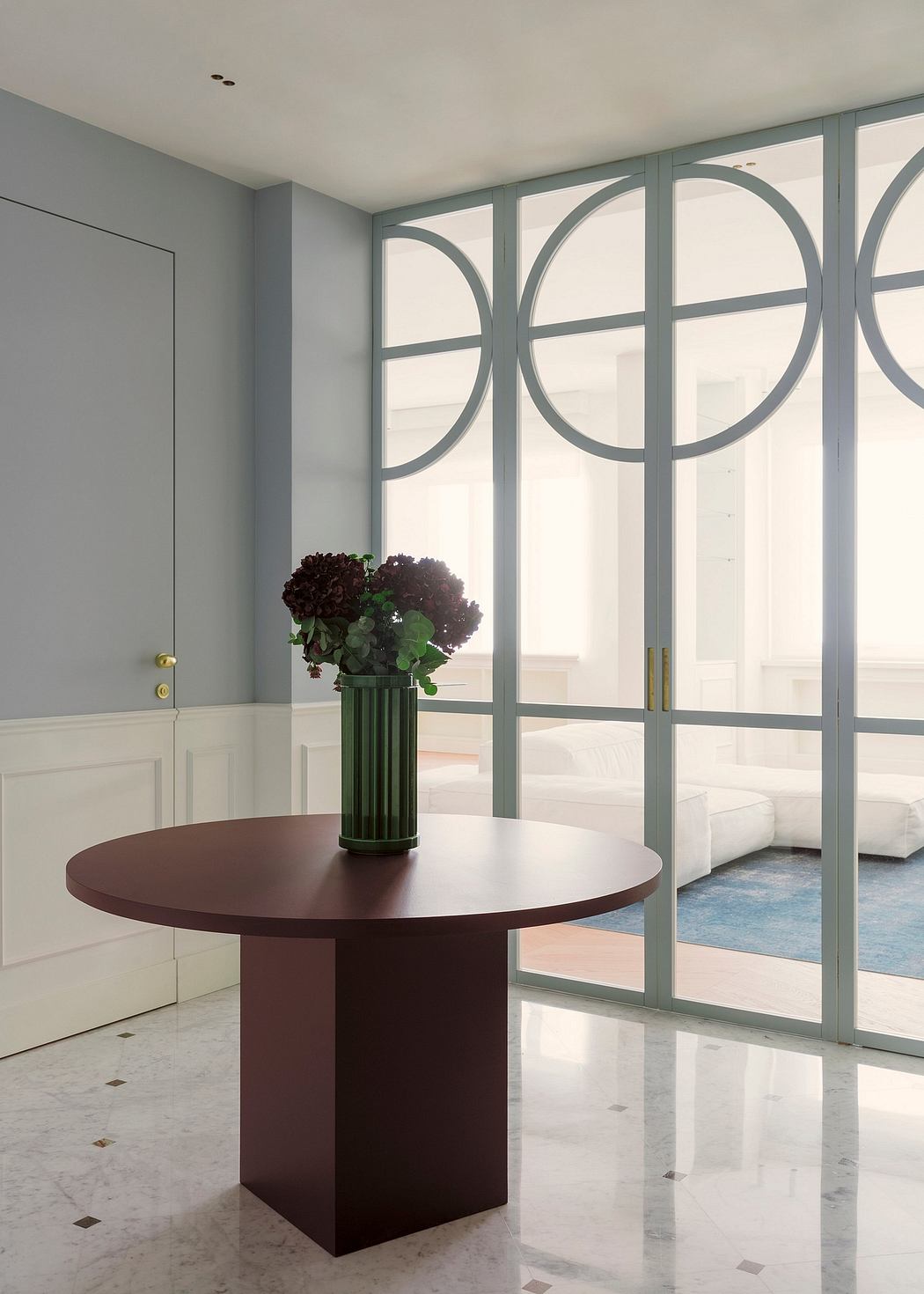 A modern entryway with arched windows, a circular dark wood table, and a potted plant.