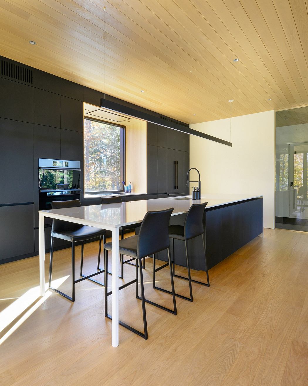 Sleek and modern kitchen with dark cabinets, wooden ceiling, and large windows.