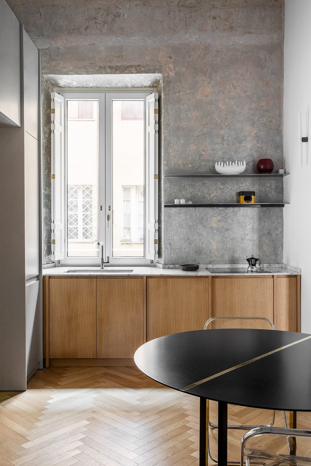 Minimalist kitchen with wooden cabinetry, exposed stone walls, and a sleek black dining table.
